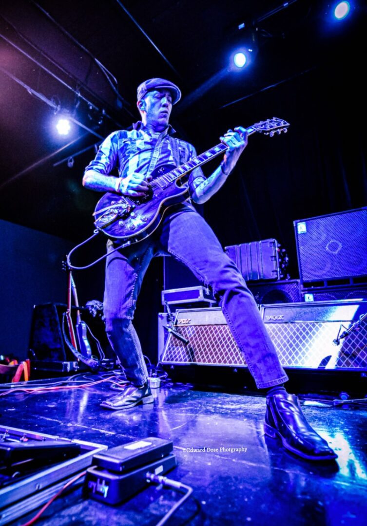 A man in blue jeans and boots playing guitar.